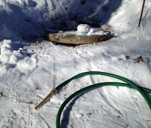 High-pressure water jetting service with a hose connected to a hole in the snow, showcasing effective snow removal techniques.