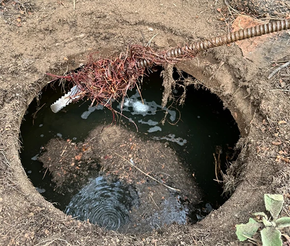 Hole in the ground with a hose and pipe, illustrating cleaning and repair services for efficient drainage solutions.