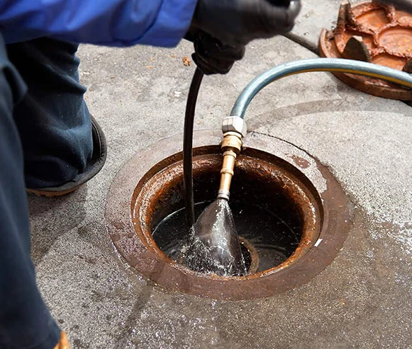 Man using a hose to clean a drain, showcasing professional hydro jetting services for effective drainage solutions.
