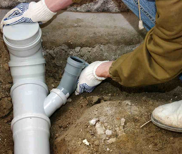 A man in gloves repairs a pipe, showcasing expertise in emergency sewer line repair services.